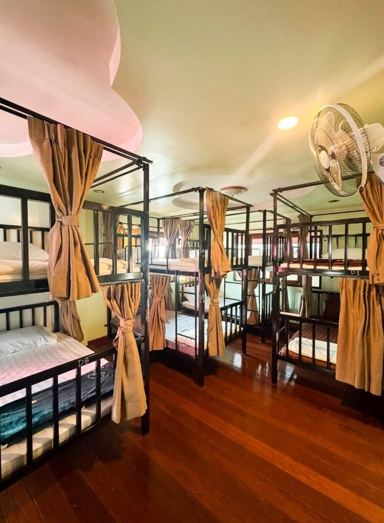 Dorm room with bunk beds, privacy curtains and a polished wooden floor.